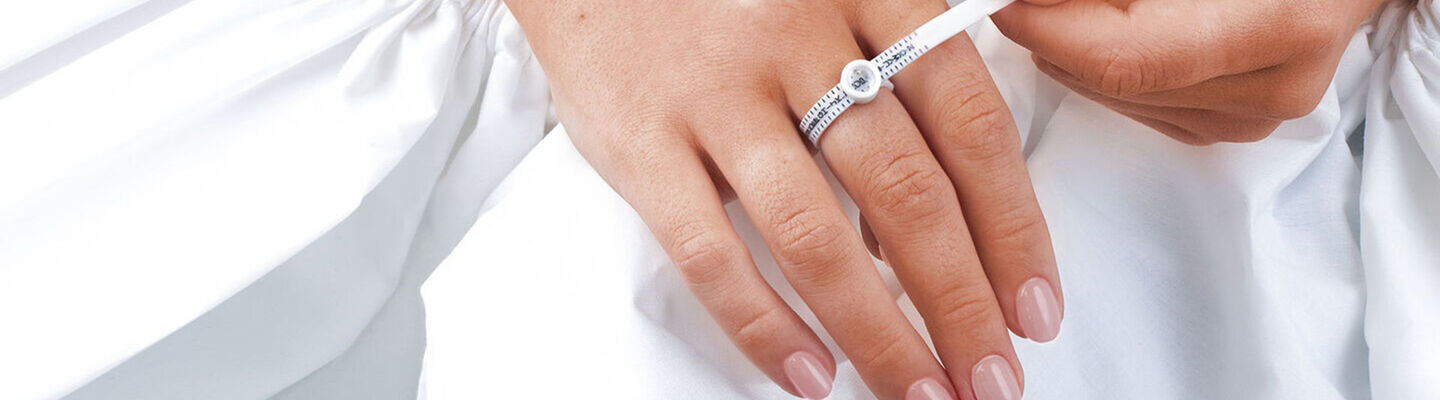 Woman using a white ring sizer tool to measure her ring finger size at home